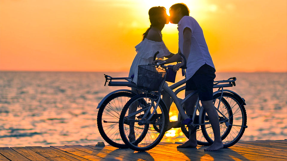 man and woman kissing by bicycle at sunset