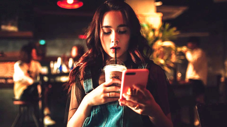 mulher tomando café com o celular na mão