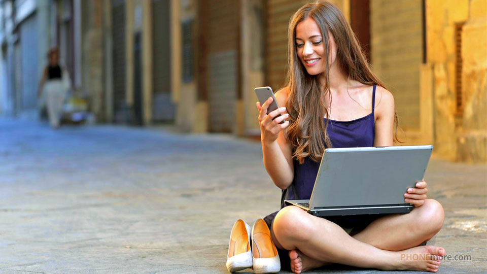 woman sitting on the street with laptop and holding a phone