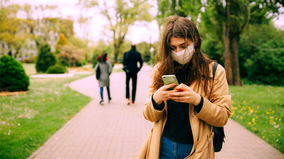 mulher no parque com o celular e máscara para se proteger do coronavírus