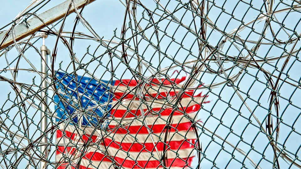 a prison wall with barbed wires and the US flag in the background