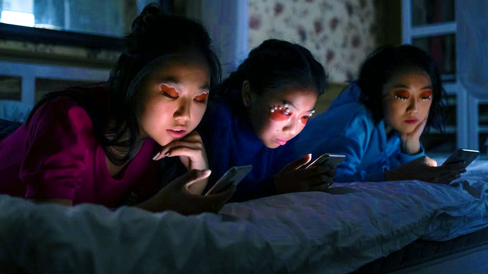 3 girls lying on the bed looking at the smartphone in the dark