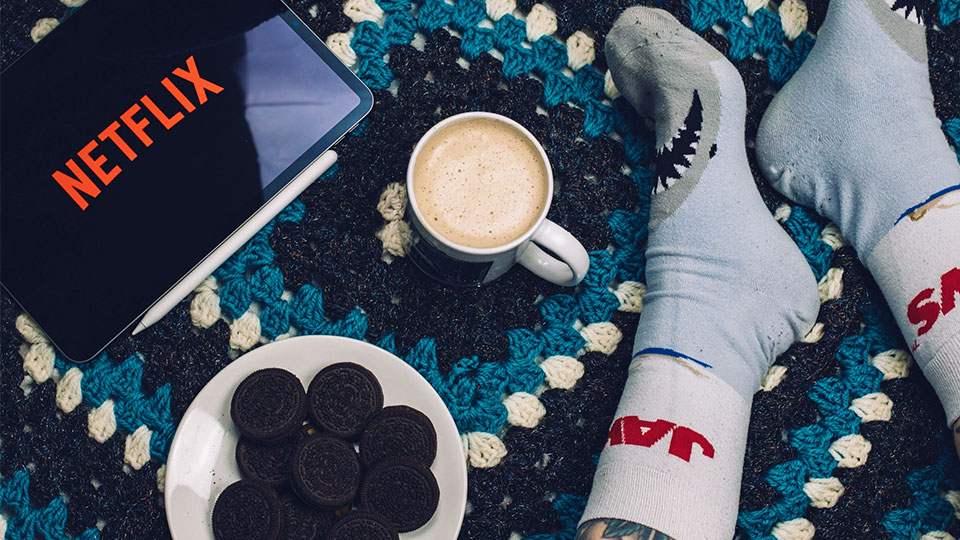 sur le sol, une tablette avec netflix, des cookies, du café et des pieds avec des chaussettes