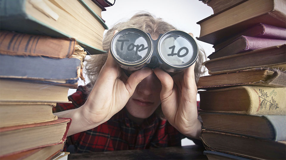 person with binoculars looking through stacked books