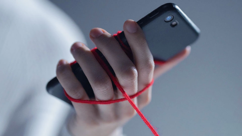 a hand holding a smartphone tied with red ropes