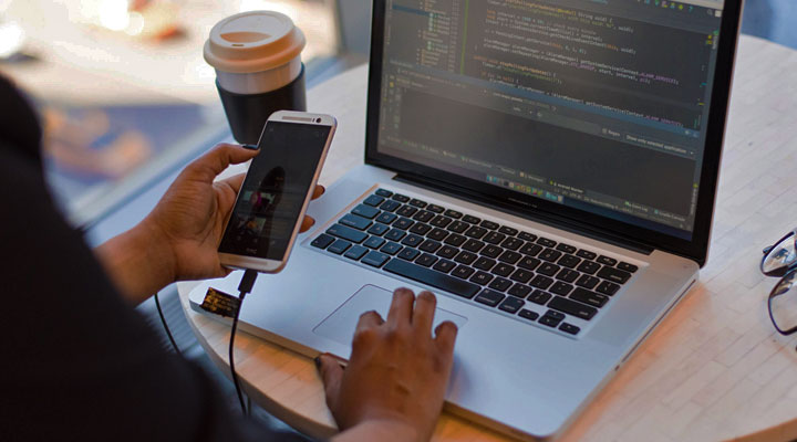 a person with a cell phone and laptop developing an app