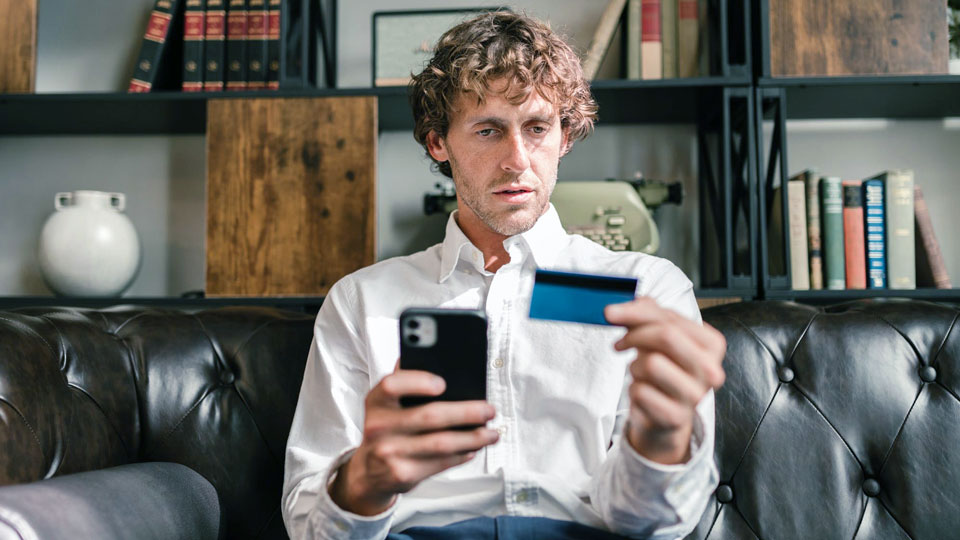 homme assis sur un canapé tenant une carte de crédit et un smartphone