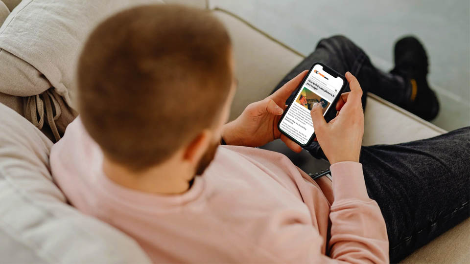 man sitting on couch looking at phonemore.com on his smartphone