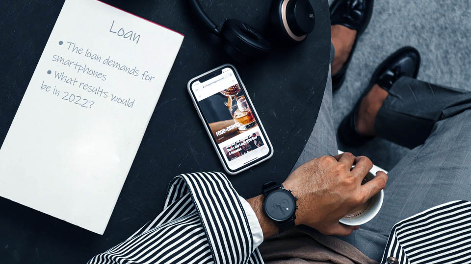 smartphone on the table next to a man sitting with a cup of coffee in his hand