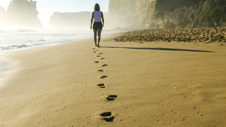a woman walking on the beach leaving footprints
