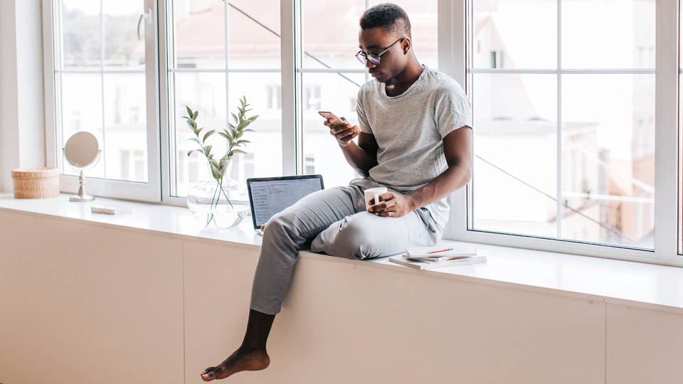 un homme assis avec un iphone à la main et un ordinateur portable à côté de lui