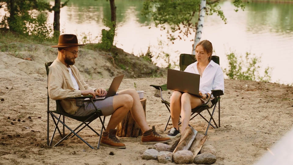 a man and a woman camping and using a laptop