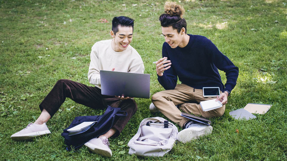 2 students on the grass with laptop and tablet