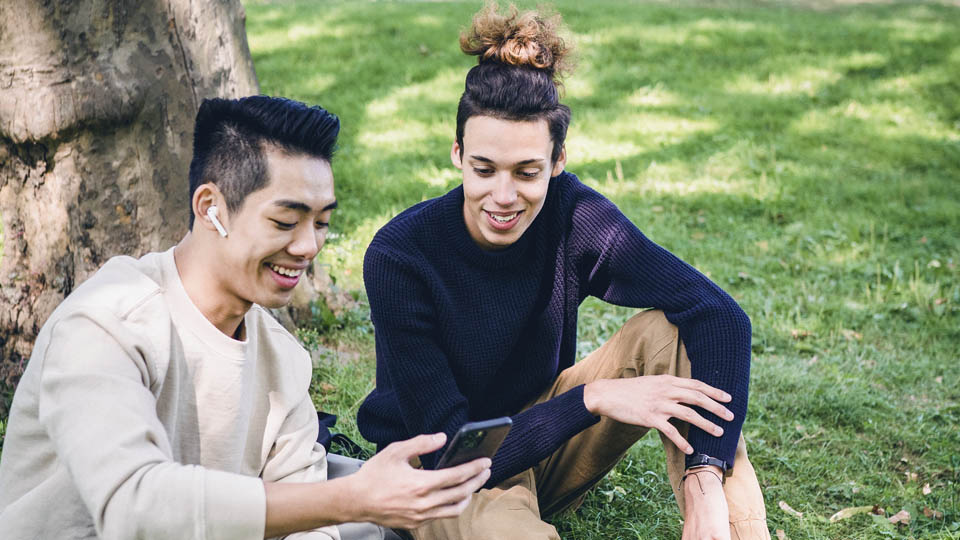 2 students sitting on the grass looking at a smartphone