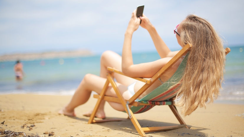 una mujer sentada en una silla en la playa con su móvil