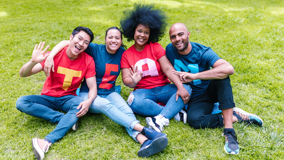 4 people sitting on the grass with t-shirts forming the word team