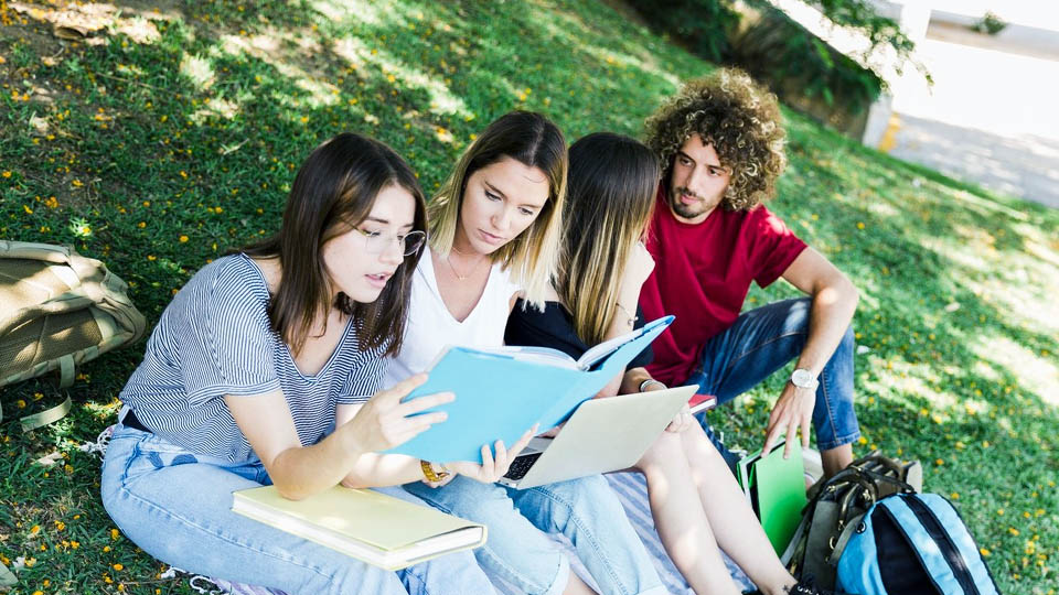 students sitting on grass with laptop and books