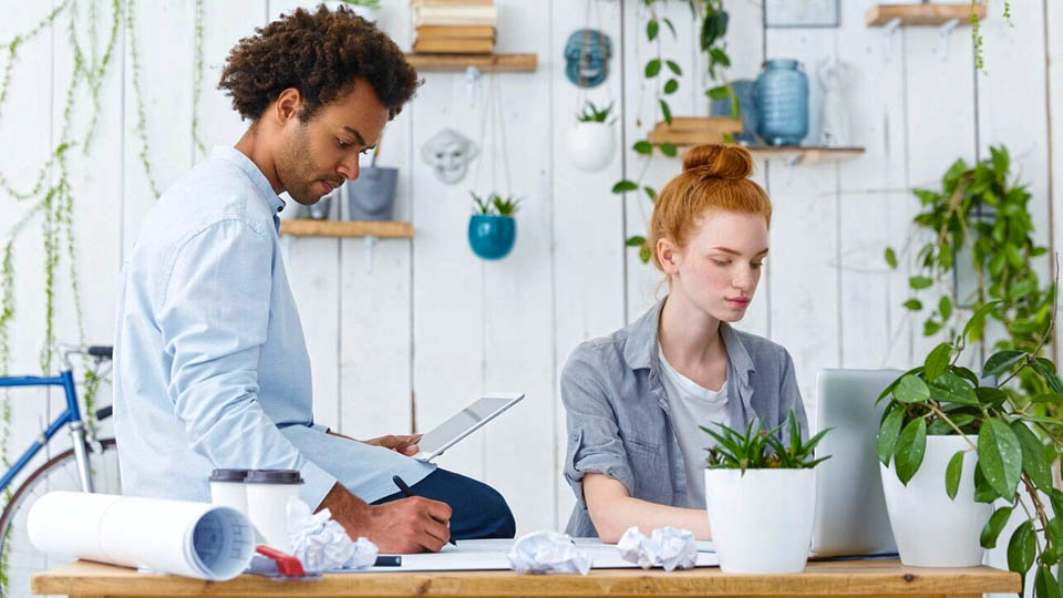 a man with a tablet and a woman working on the laptop