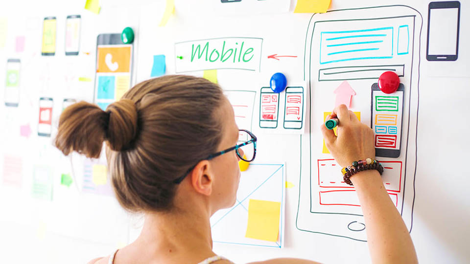 a woman drawing mobile application prototypes on a whiteboard