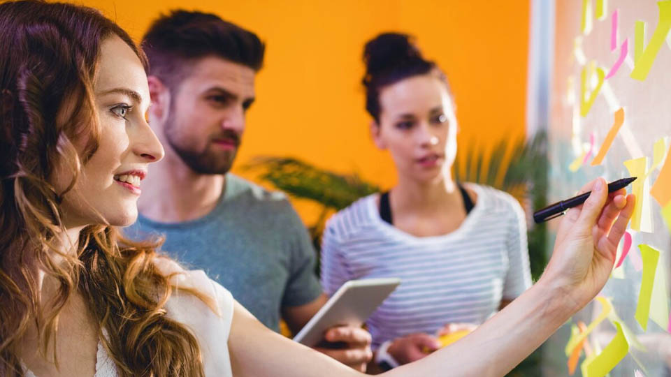 three people looking at a mobile project on a post-it board