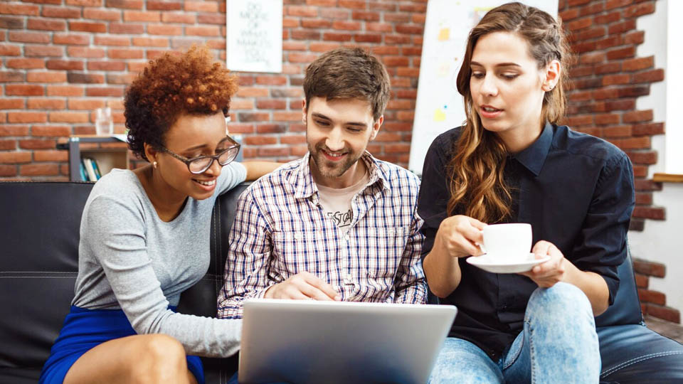 three people sitting on the sofa looking at a website on the laptop