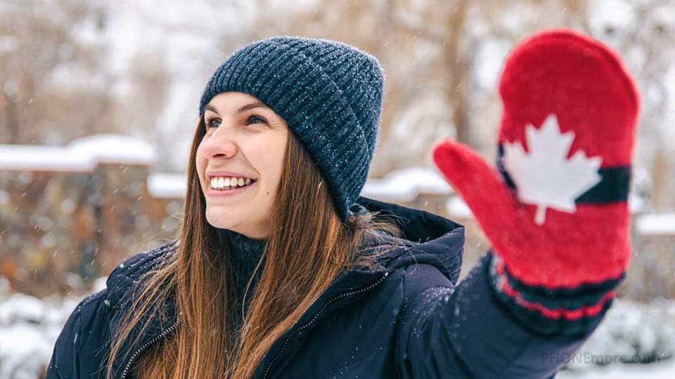 a happy woman in warm clothing showing her hand wearing a glove with the flag of canada