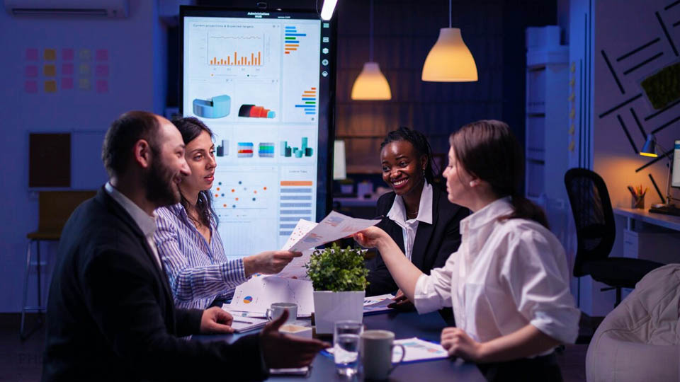 a team of 4 people at an office table with a dashboard behind them