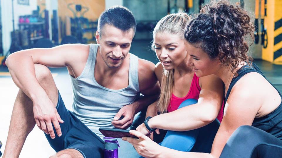 2 women and a fitness man in the gym looking at a smartphone