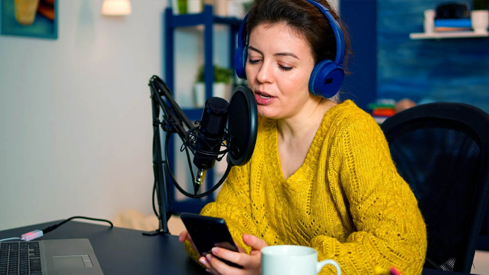 femme diffusant des émissions en direct avec un microphone et un smartphone dans un studio de baladodiffusion