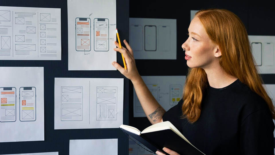 a red-haired woman looking at a wall with software development prototypes on the wall