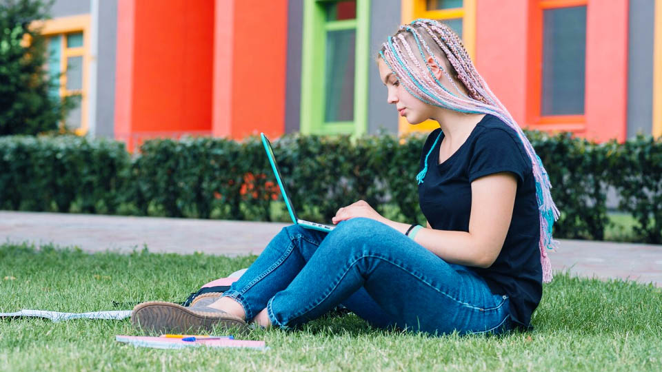 student sitting on the grass with a laptop