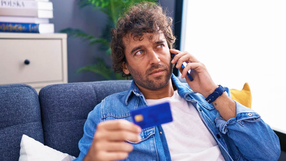 man sitting on the couch talking on the phone and holding a credit card
