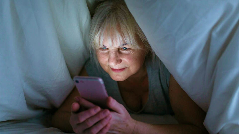 elderly woman lying in bed using her smartphone at night
