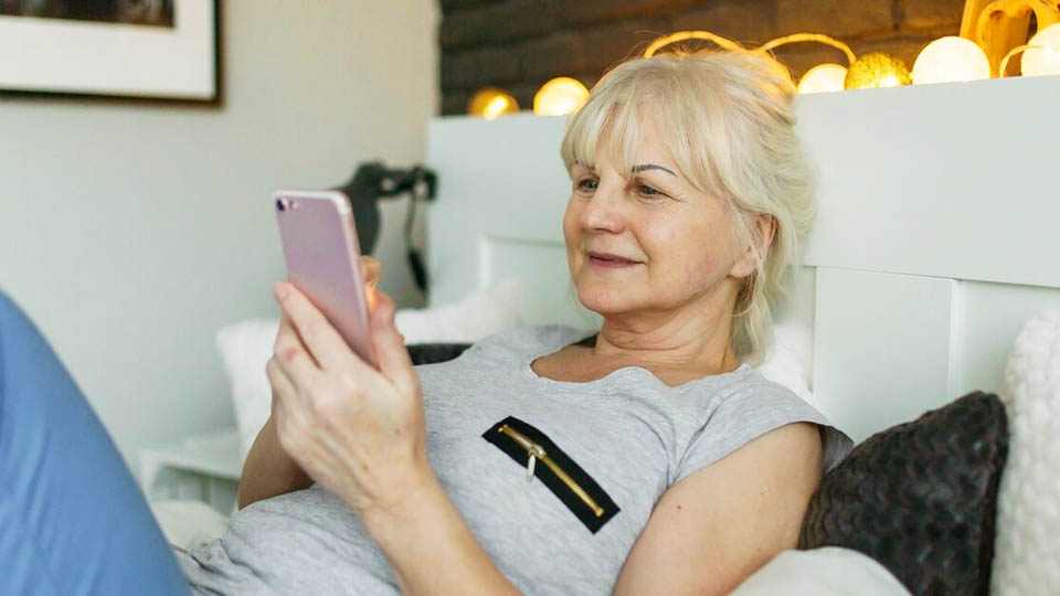 elderly woman sitting in bed using her smartphone during daytime