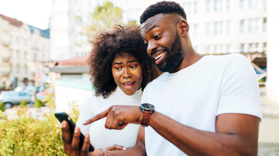 un couple en ville, à l'extérieur, semble surpris par l'écran de son smartphone