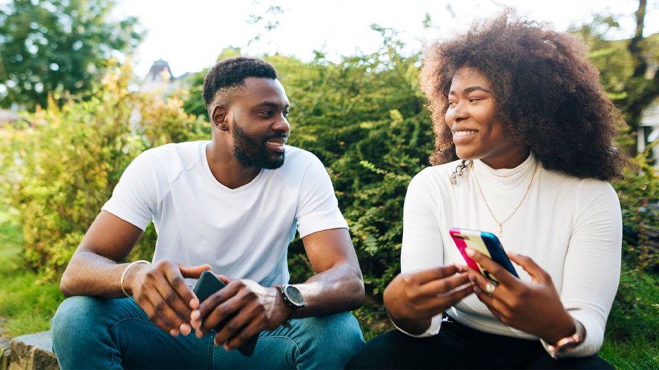 un couple souriant, assis dehors, smartphones à la main