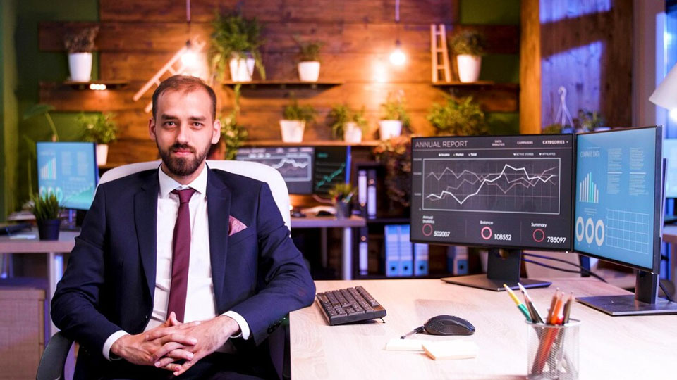 a businessman sits at his office desk with performance charts on his computer screen