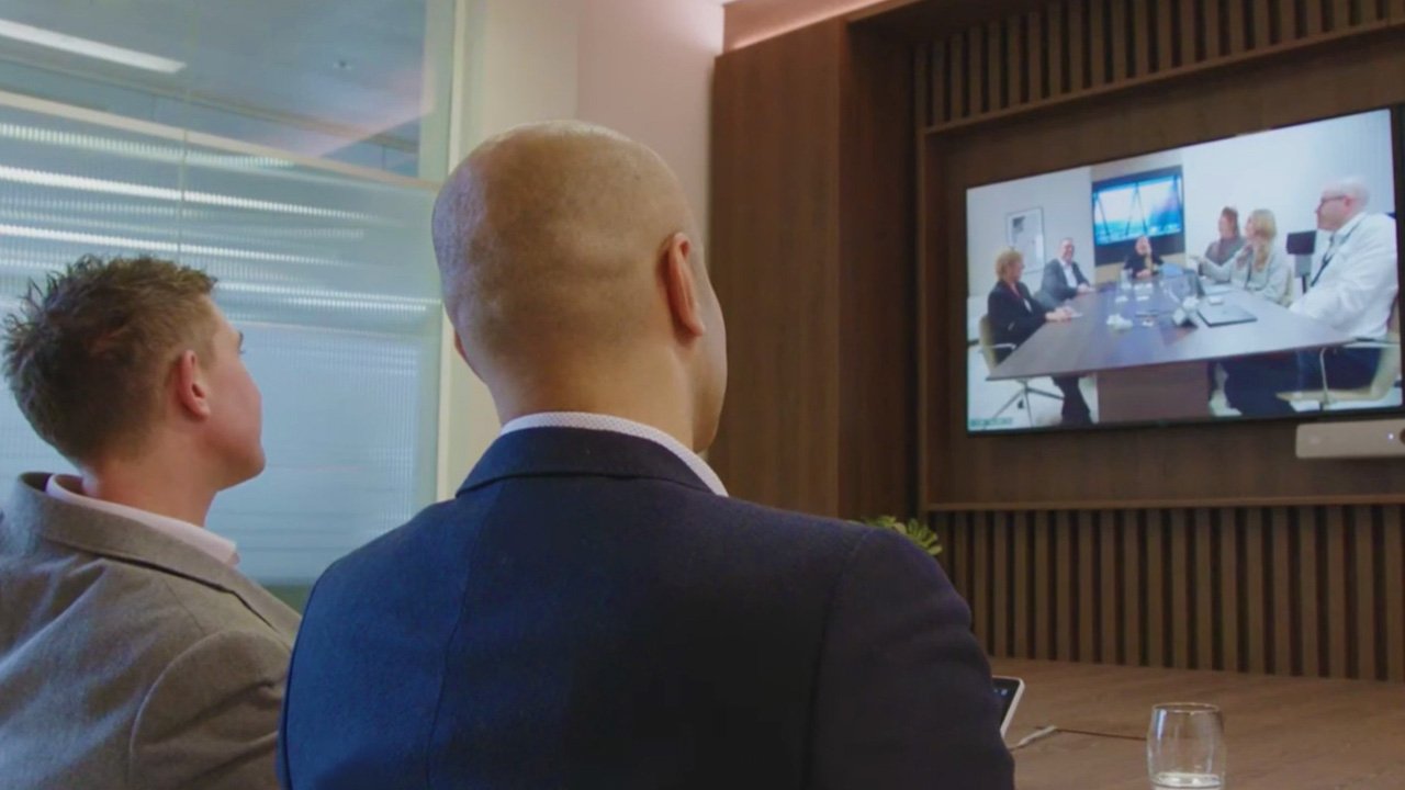 two people watching a TV while participating in a remote meeting